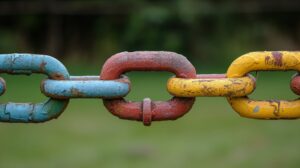 A close-up view presents a series of interlinked metal chains with remnants of colorful paint. Each link is coated in a different color, revealing signs of wear and rust, indicating age and exposure to the elements. The background is a soft, blurred green, suggesting a natural outdoor setting, possibly a playground or garden area.